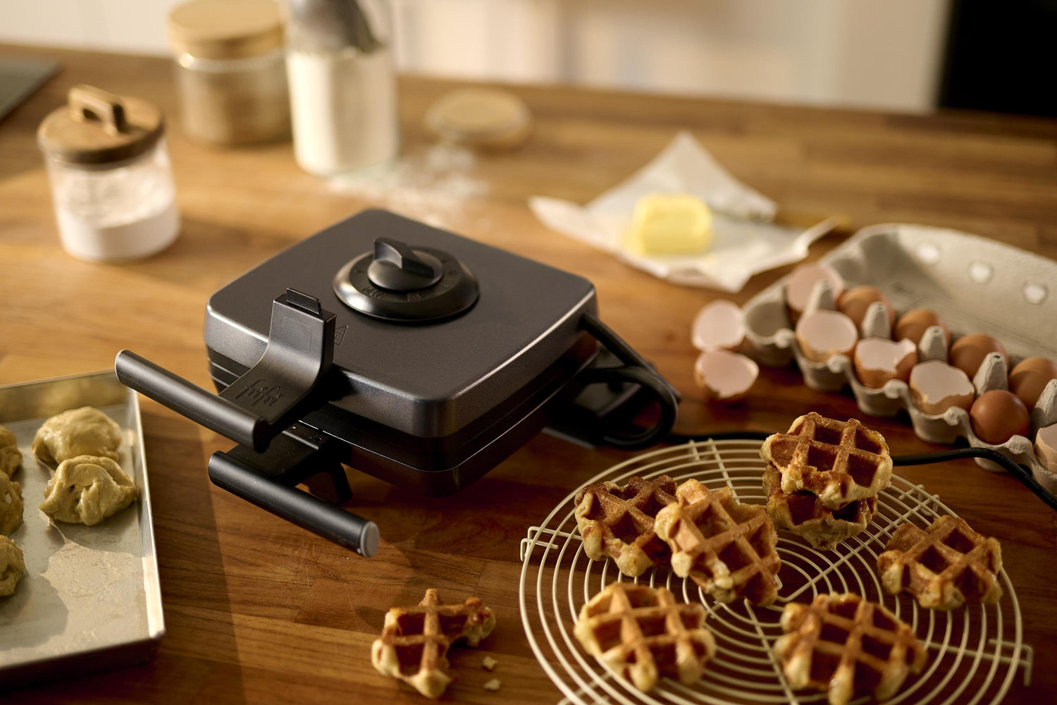 Gaufrier noir, œufs, beurre, pâte, plan de travail en bois.