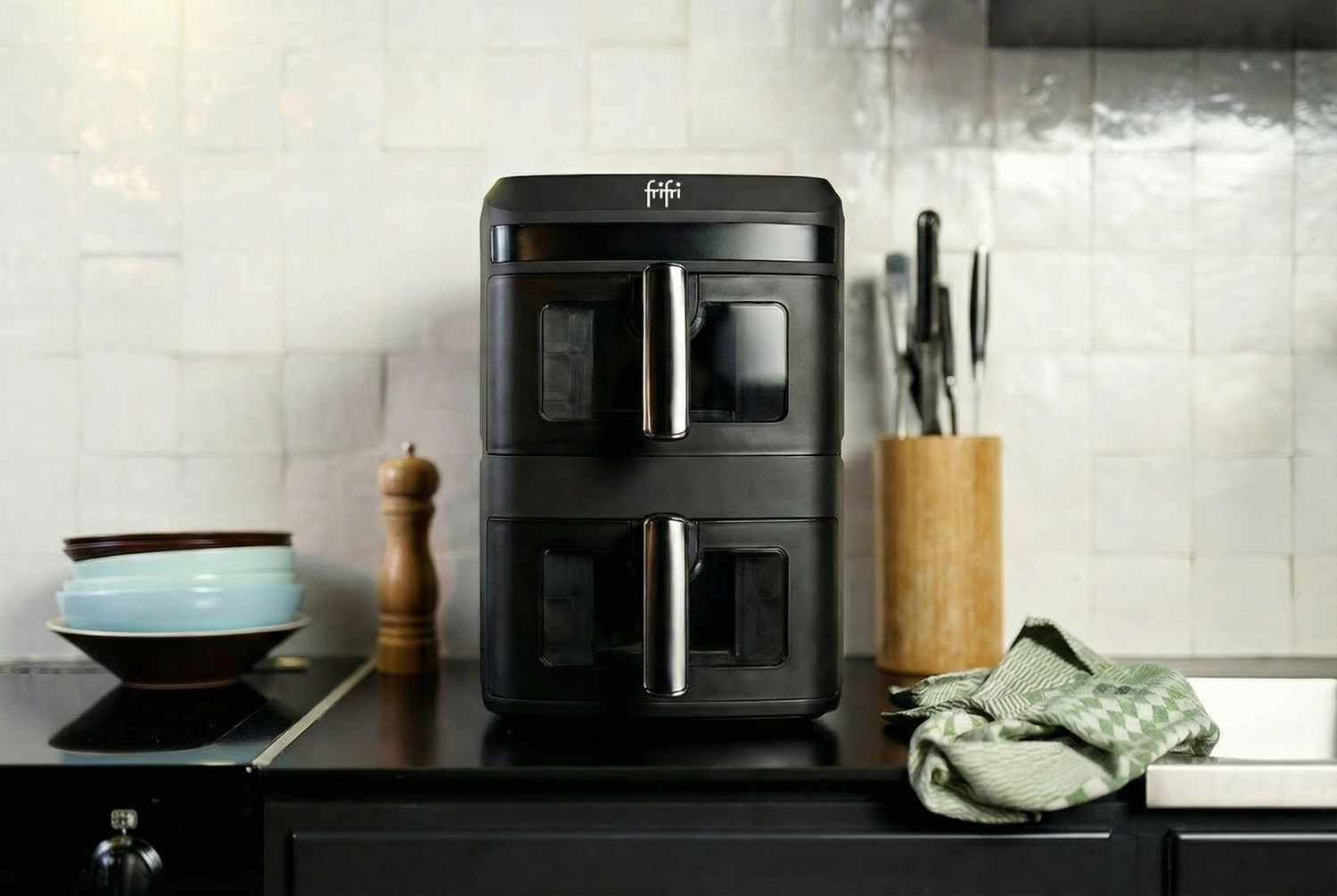 Un Airfryer Duo Slim est placé sur le comptoir d'une cuisine à côté de bols empilés, d'un moulin à poivre, d'un bloc de couteaux et d'un torchon de cuisine à carreaux verts.