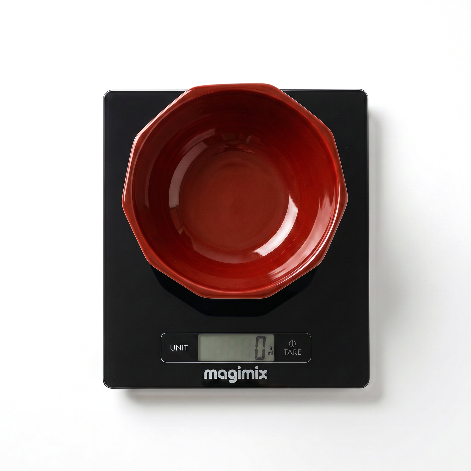 Un bol rouge est posé sur une balance de cuisine numérique noire Balance de précision affichant zéro gramme sur fond blanc.