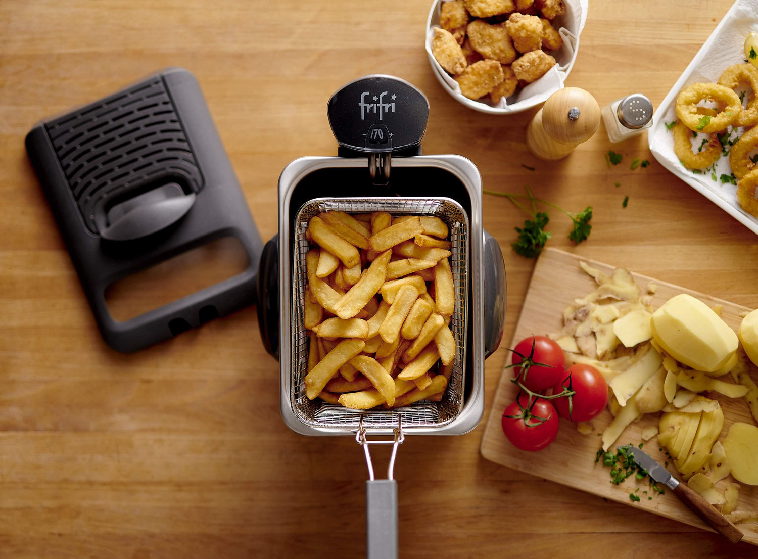 Friteuse avec frites, tomates et calmars frits sur table en bois.