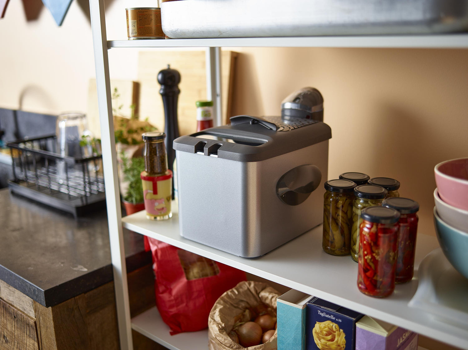 Étagère blanche avec friteuse, bocaux de légumes, pâtes et condiments.