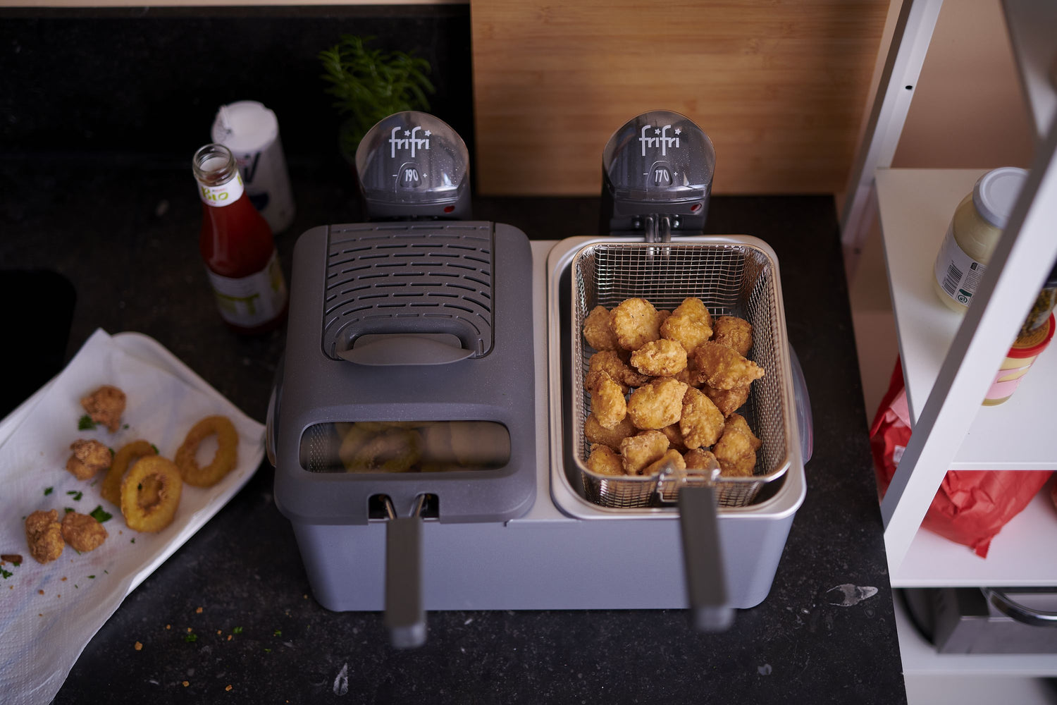 Friteuse grise double bac avec aliments frits et accessoires de cuisine.