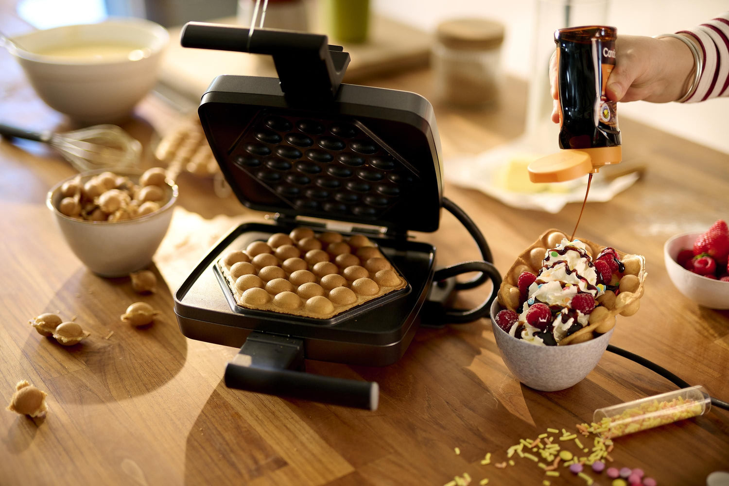 Gaufrier ouvert, gaufre à bulles, garniture et main versant du sirop.